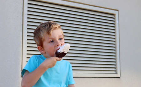 The blond boy takes a bite of ice cream and looks intently into the distance. The five-year-old has a sweet tooth.の写真素材