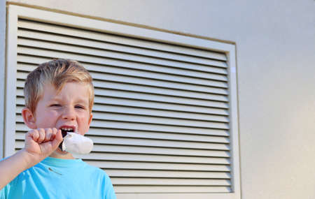 The blond boy squinted his eyes and licked the ice cream. A five-year-old boy shows grimaces.の写真素材