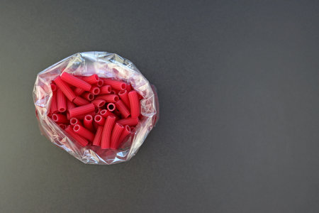Red Tubetti Rigati pasta in a bag on a gray background. Beet Pasta in the form of small tubes.の写真素材