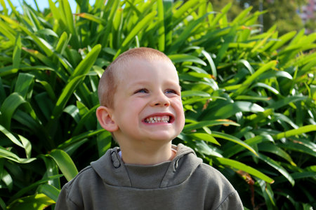 The short-haired, blond boy looks up and smiles, showing all his teeth. A five-year-old boy with a grin on his face.の写真素材