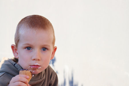 A short-haired, blond boy with a dirty face stares into the distance, spellbound. A thoughtful five-year-old boy against a light background.の写真素材