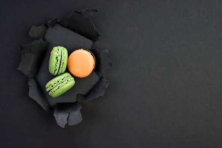 Green and beige macaroons on a background of black torn paperの写真素材