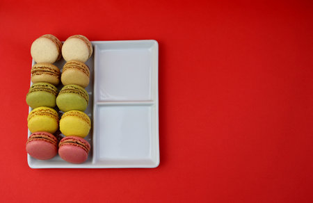 Multicolored macaroons in a white square plate on a bright red background.の写真素材