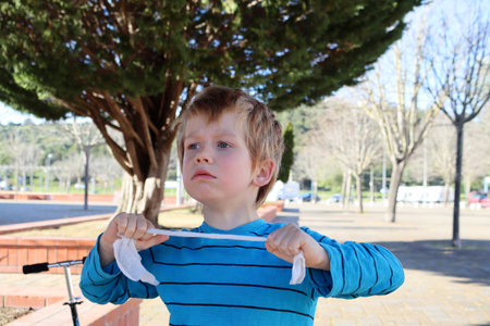 A disgruntled blond boy pulls a white rope with his hands. A five-year-old boy is in a bad mood.の写真素材