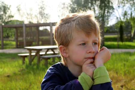 A blond boy with sad eyes looks into the distance. A pensive five-year-old boy in the rays of the sun.の写真素材