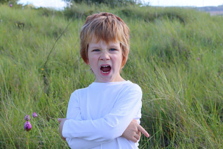 The blond boy furrowed his nose and opened his mouth wide. five year old boy in a bad mood.の写真素材