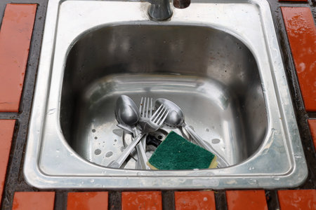 Dirty spoons and forks lie in the sink along with the dishwashing sponge.の写真素材