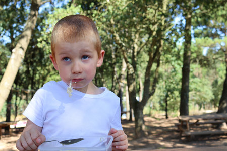 A blond boy with noodles in his mouth rolls his eyes and looks into the distance. Disgruntled six year old boy.の写真素材