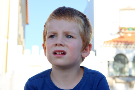 A six-year-old boy furrowed his brows and looks thoughtfully into the distance. Portrait of a blond boy on the background of the old city.の写真素材