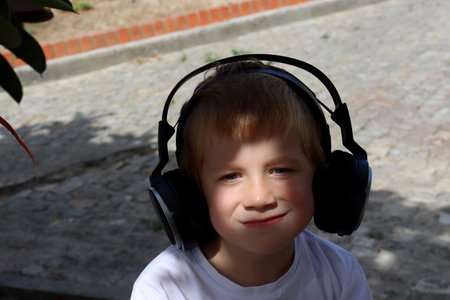 Portrait of a cute boy listening to music on headphones and smiling. Young music lover in the shade of treesの写真素材