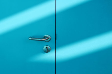 Close up of a light blue door with a metal handle and shadow on the wallの写真素材