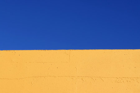 Part of a yellow wall against a blue sky. Blue and yellow, divided into two parts backgroundの写真素材
