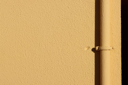 Light yellow concrete wall with pits and roughness, vertical pipe and small fitting with rivets. High resolution with large copy space and detailの写真素材