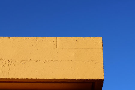 Section of a yellow wall contrasting with a clear blue sky. Geometric exterior architecture in minimalist style. building detailの写真素材