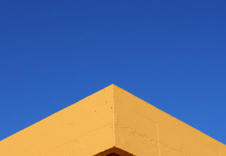 corner of yellow wall against blue sky background in symmetric view, Geometric exterior architecture in minimal style. detail of a buildingの写真素材