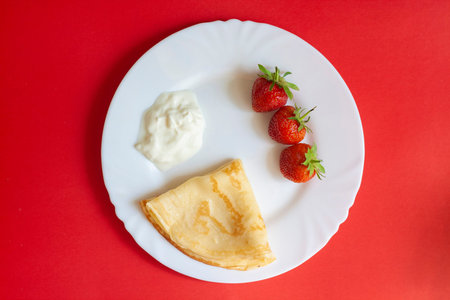 Breakfast, strawberries, pancakes and cream on a white plate on a red background