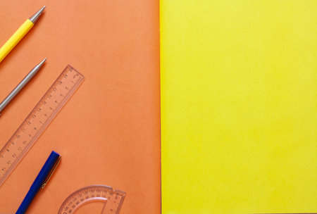 Layout of office supplies on an orange and yellow background, pens and rulers, top view, copy space