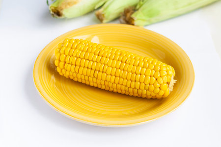 Boiled corn on a yellow plate raw corn in the background