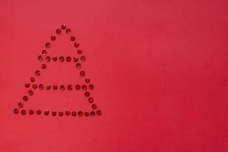 Christmas tree is laid out in red shiny sequins on a red backgroundの写真素材