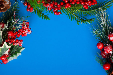 Christmas layout of spruce branches red berries and cones on a blue background flat lay copy space