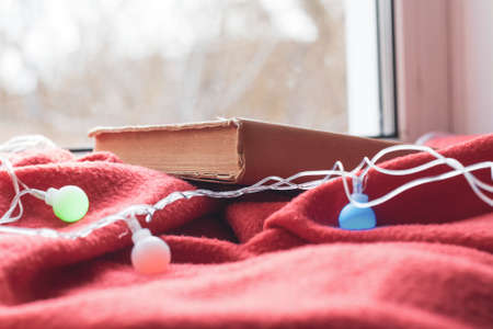 Autumn mood window and window sill with red blanket book and garland with lightsの写真素材