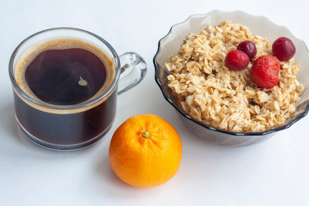 Breakfast on white background oatmeal with berries coffee and fruit and tangerine