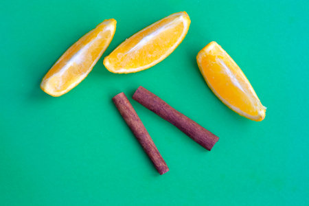 Orange slices and cinnamon sticks on a green background flat lay