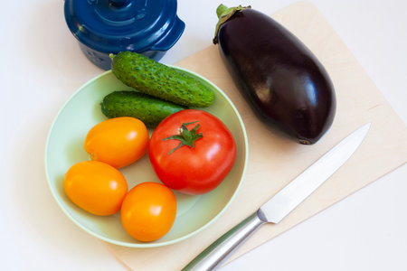 Cooking vegetables tomatoes and cucumbers in a plate eggplant pot cutting board and knife