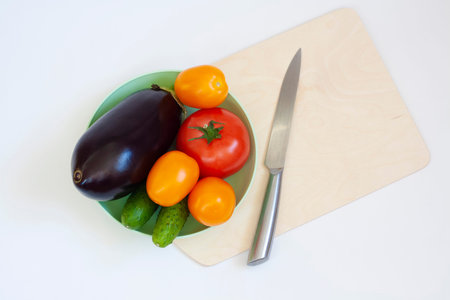 Cooking vegetables tomatoes and cucumbers in a plate eggplant cutting board and knife