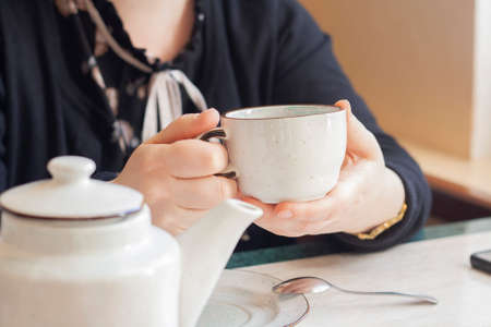 White cup of tea in the hands of a woman teapot restaurantの写真素材