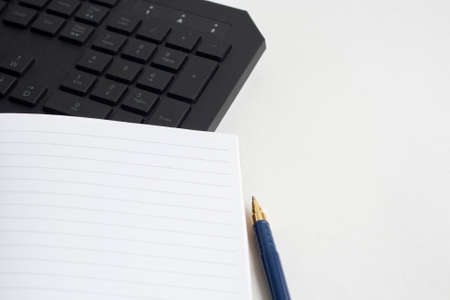 Workplace computer keyboard notebook for writing and blue penの写真素材