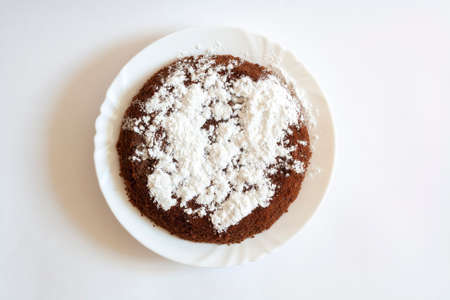 Chocolate sponge cake with powdered sugar on a plate isolated on a white backgroundの写真素材