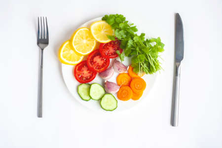 Summer menu a plate of fresh vegetables a fork and a knife on a white background flat layの写真素材
