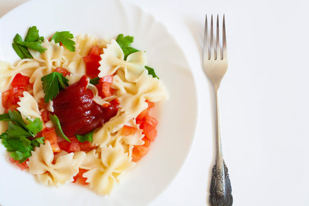 Pasta farfalle with tomatoes herbs and sauce in a plate and fork on a white background