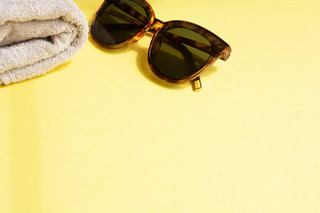 Sunglasses and towel on a yellow background copy space