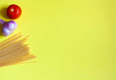 Cooking pasta with tomato and garlic on a yellow background flat lay copy spaceの写真素材