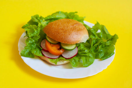 Vegan burger with vegetables on a white plate on the yellow background
