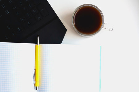 Workplace, computer keyboard coffee open notebook and pen on a white background copy space