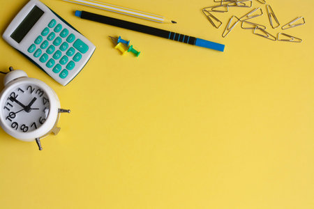 Alarm clock calculator and stationery on a yellow background copy space