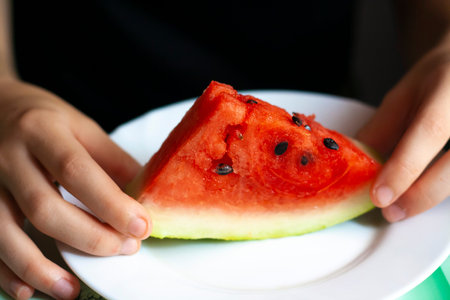 A piece of ripe watermelon in the girl's hands on a white plate