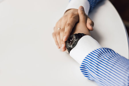 hands of a man in a wristwatch on a white tableの写真素材