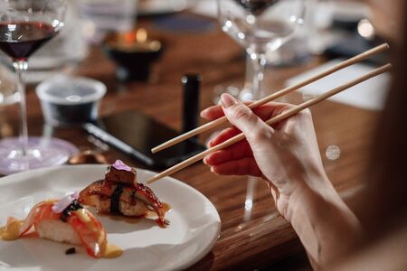Girl eats sushi with Chinese chopsticks at a table in a restaurant. Close-up of handsの写真素材