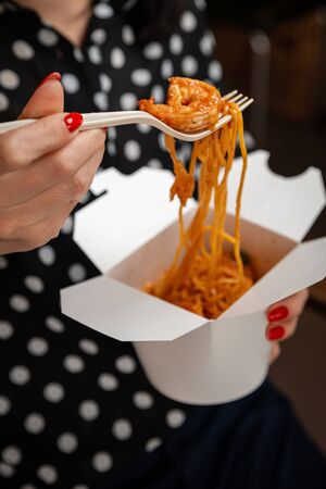 Girl eats pasta with shrimp from a white box with a fork. Close-upの写真素材