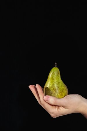Girl holds a pear. Close-up hand on a black backgroundの写真素材