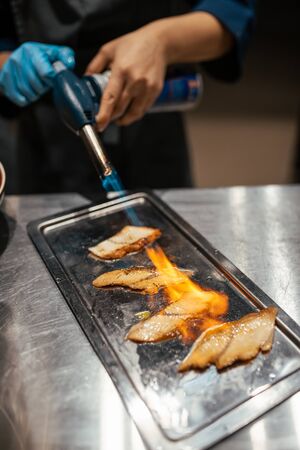 Chef cooks fish using a using gas burner torch. Flambe gun pistol. Flamming fishの写真素材