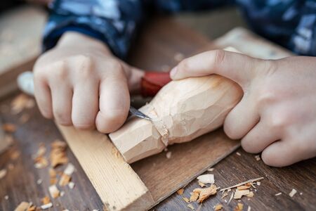 child carves a toy in wood with a knife.  carpenter in the workshop. Close-up of hands の写真素材