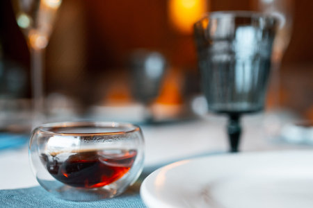 a transparent bowl with black tea on a table in a restaurant. Close-up, blurred background.