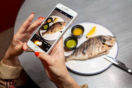 A woman photographs food on the phone in a restaurant. Close-up of handsの写真素材