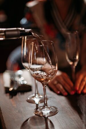 The waiter pours wine into a glass in a restaurant. Close-up, natural light . Shallow depth of fieldの写真素材