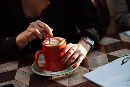 Girl in a cafe with a mug of hot drink. Close-up of hands and mug with cappuchino, lifestyleの写真素材